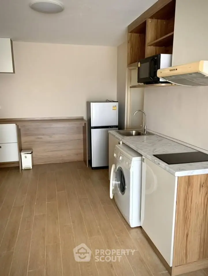 Modern kitchen with wooden flooring, washing machine, fridge, and microwave in compact layout.