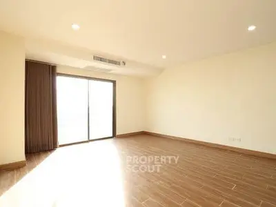 Spacious empty living room with wooden flooring and large window for natural light.