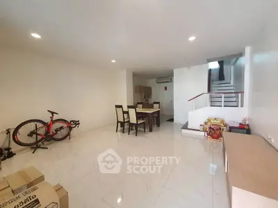 Spacious modern living room with dining area and staircase, featuring sleek tile flooring and minimalist decor.
