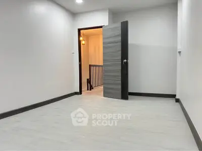 Spacious empty room with modern flooring and open door leading to hallway