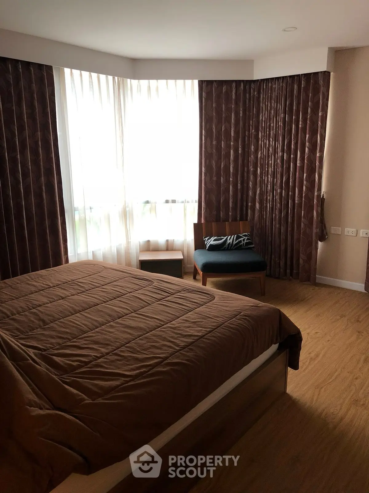 Cozy bedroom with large window and elegant brown curtains, perfect for relaxation.