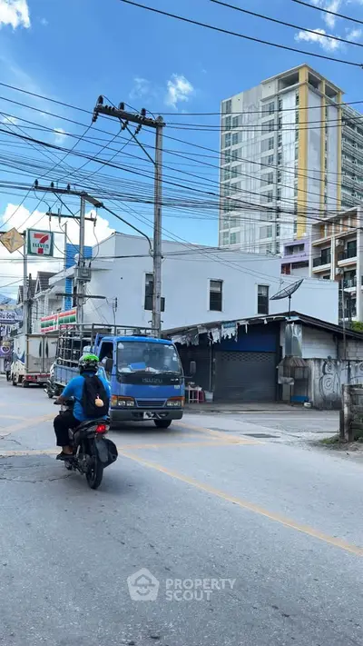 Urban street view with residential building and commercial area under clear blue sky.