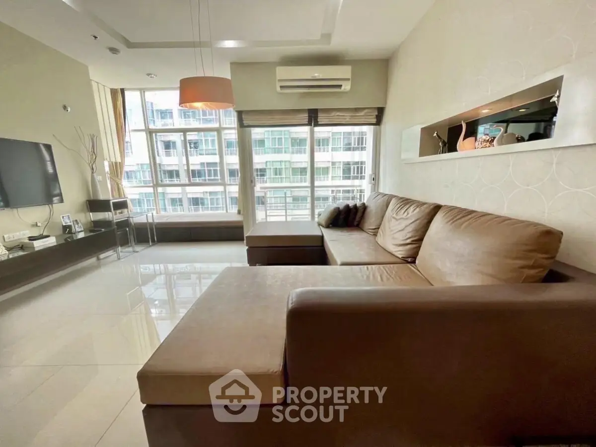 Spacious modern living room with large windows and comfortable seating in a high-rise apartment.
