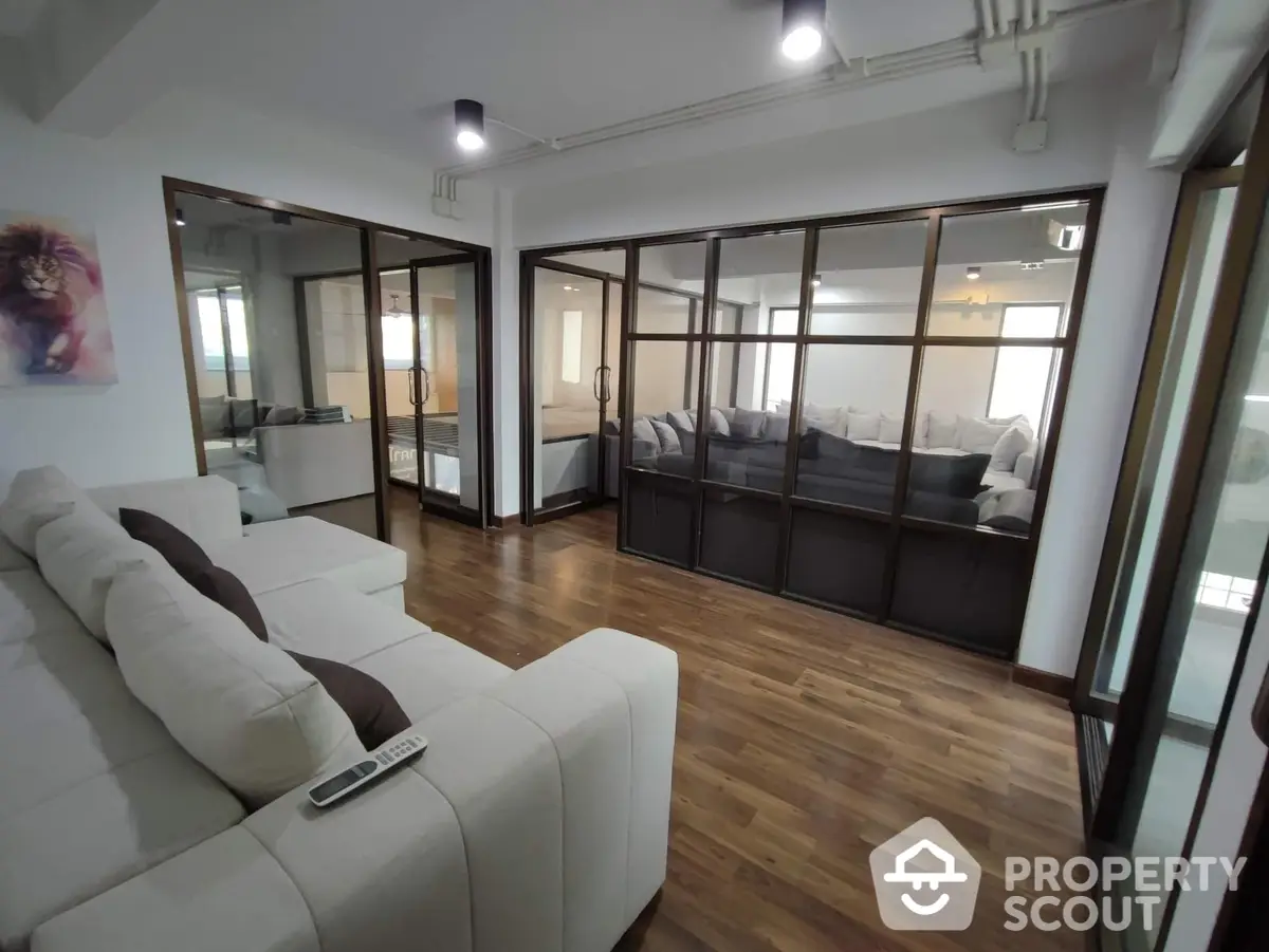 Spacious living room with elegant hardwood flooring, modern lighting, and large glass partition doors leading to an adjacent room, creating an open and airy atmosphere.