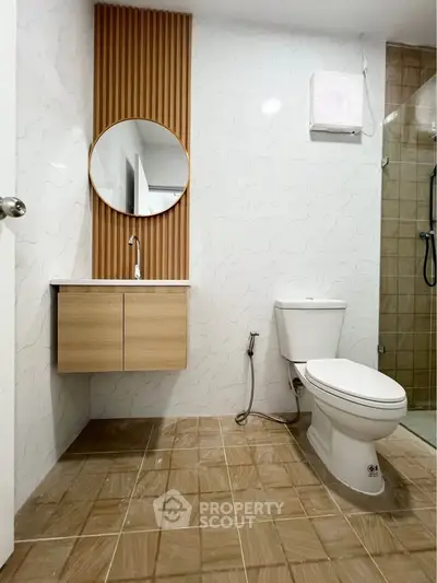 Modern bathroom with stylish vanity and round mirror, featuring a sleek shower area.