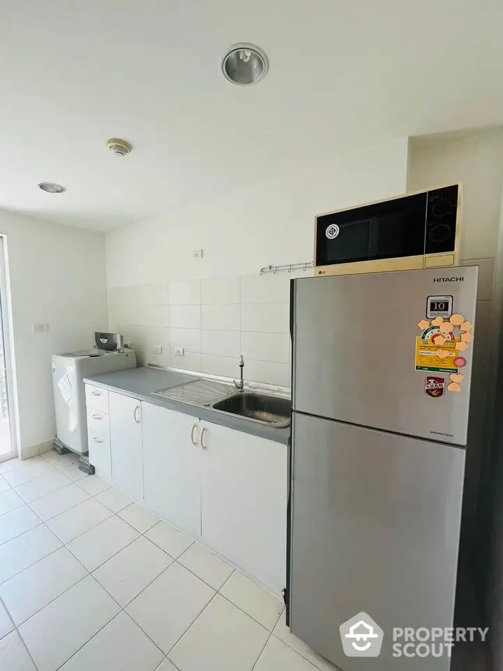 Modern kitchen with fridge, microwave, and washing machine in bright apartment.