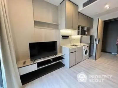 Modern apartment interior with sleek kitchen and living area featuring washing machine and TV setup.