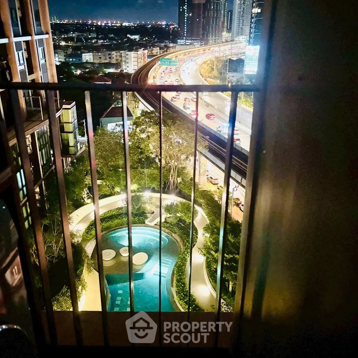 Stunning city view from high-rise balcony overlooking illuminated pool and highway at night.