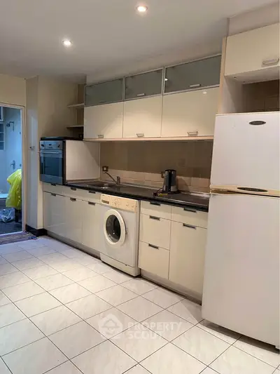 Modern kitchen with sleek cabinets, washing machine, and built-in oven in a cozy apartment.