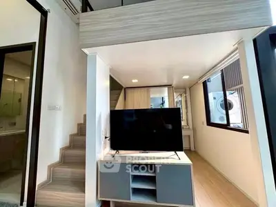 Modern loft-style living room with TV and staircase, featuring sleek design and ample natural light.