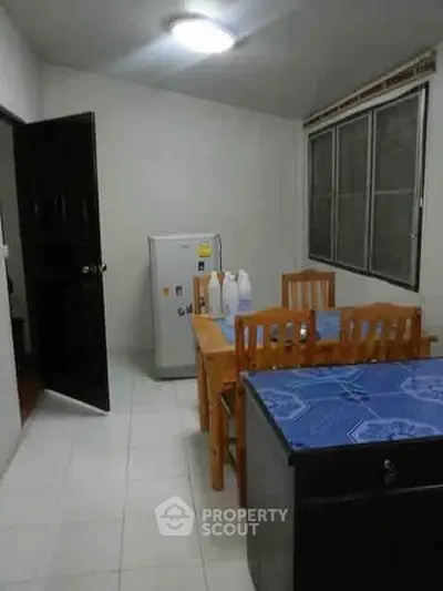 Cozy dining area with wooden table and chairs, compact fridge, and tiled flooring.