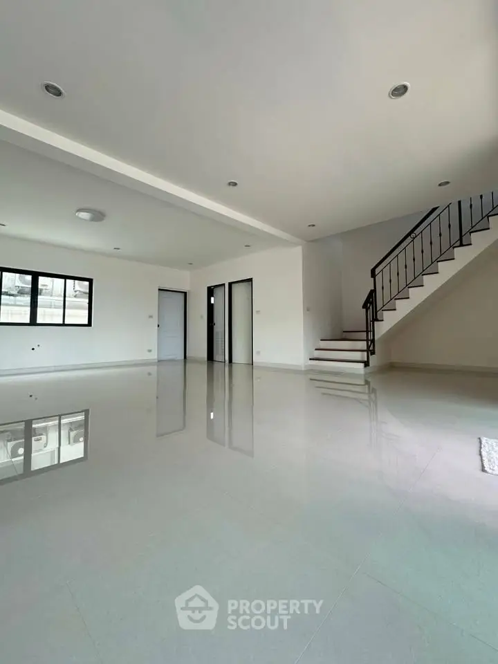 Spacious modern living room with glossy floors and staircase, ideal for family gatherings.