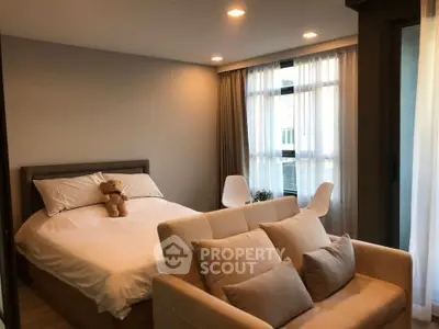 Cozy bedroom with plush bed, soft lighting, and modern decor, featuring a small sofa and large windows.