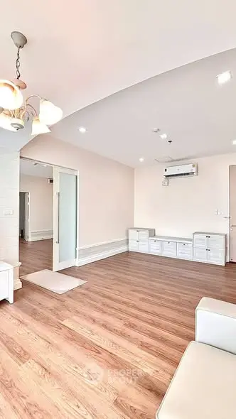Spacious living room with wooden flooring and modern lighting in a bright apartment.
