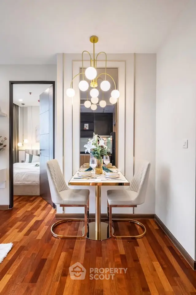 Elegant dining area with modern chandelier and wooden flooring, adjacent to a cozy bedroom.