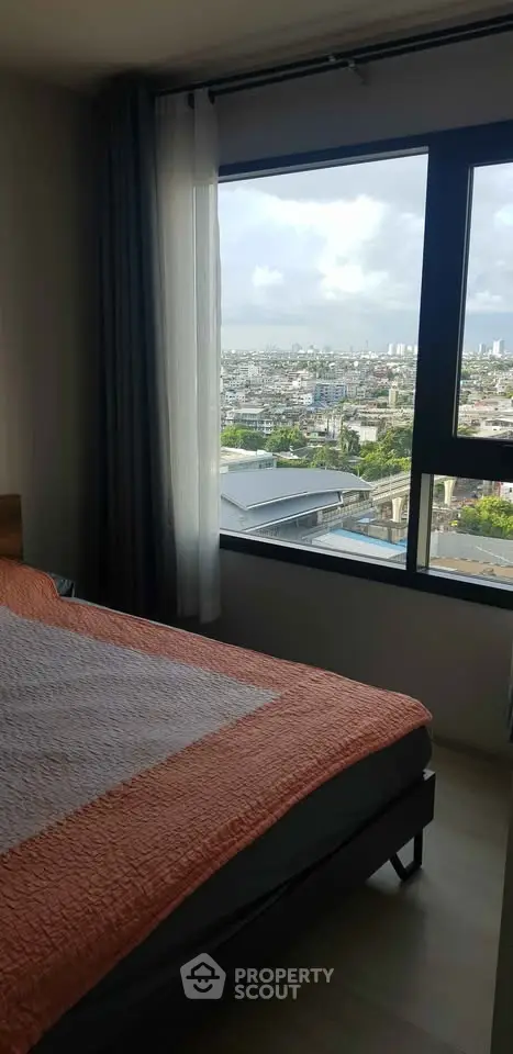 Cozy bedroom with large window offering stunning cityscape views, perfect for urban living.