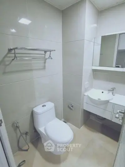 Modern bathroom with sleek fixtures and neutral tiles, featuring a toilet, sink, and mirror.