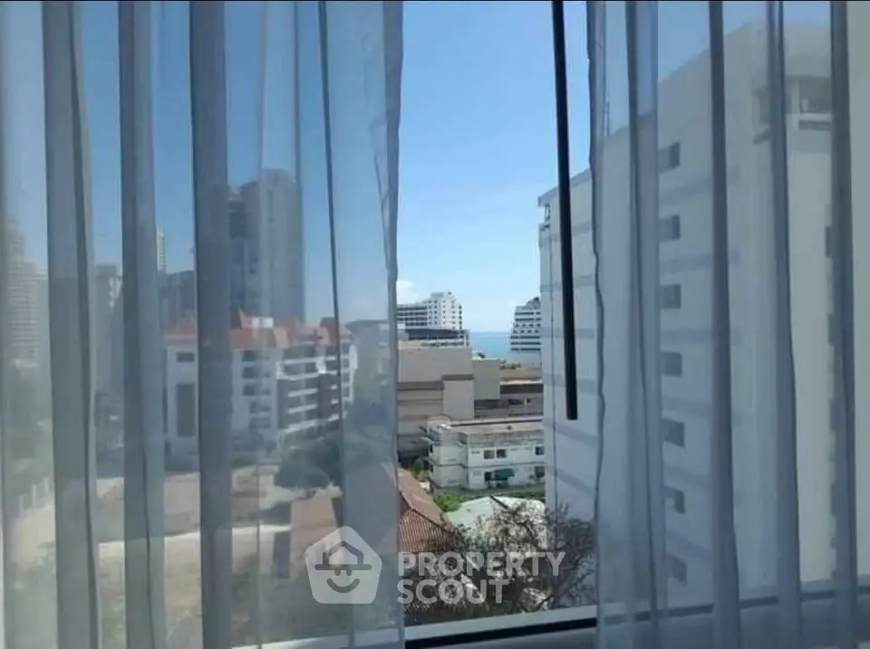 Stunning urban view from a window with sheer curtains, showcasing cityscape and blue sky.