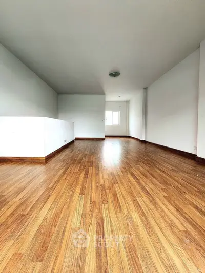 Spacious empty room with wooden flooring and white walls, ideal for customization.