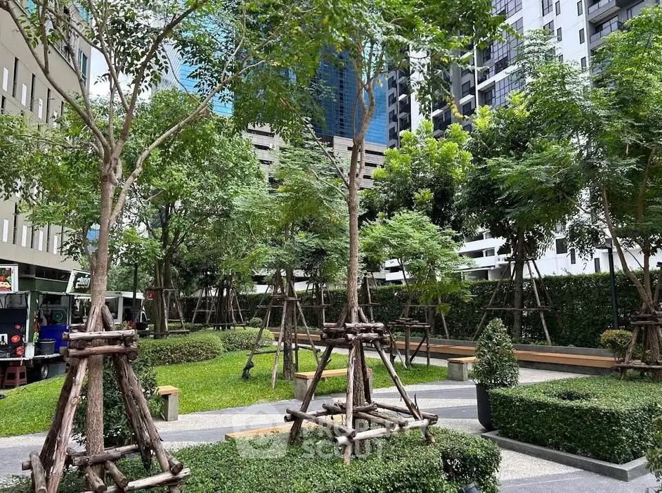Lush green garden area in modern residential complex with tall trees and manicured hedges.
