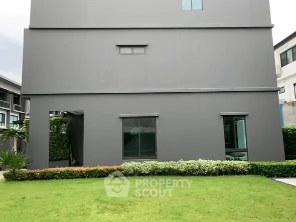 Modern gray building exterior with lush green lawn and shrubs