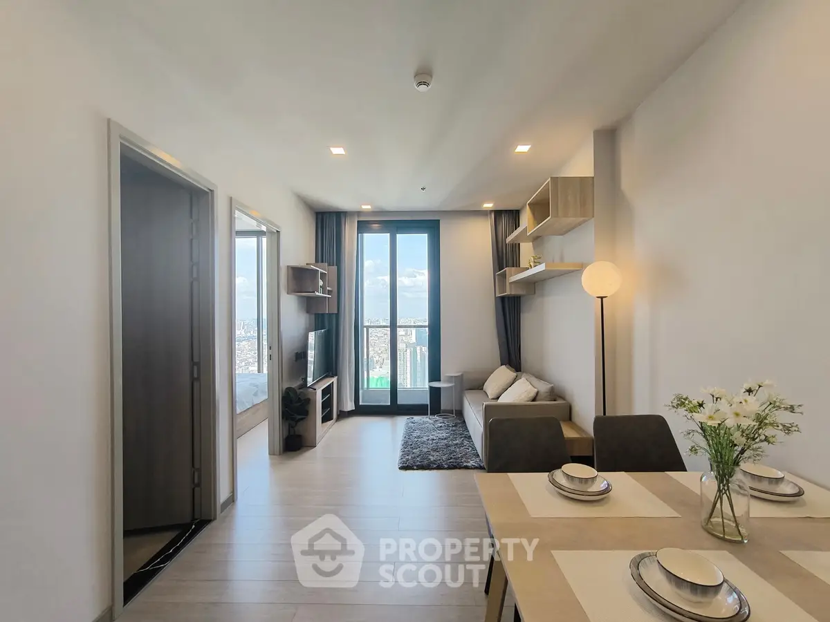 Modern open-plan living room with dining area and city view balcony in a stylish apartment.