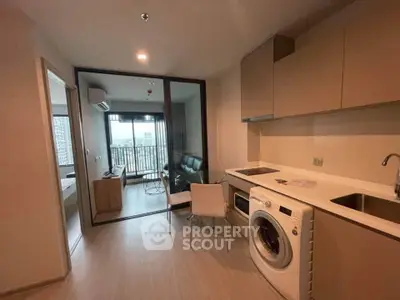 Modern apartment with open kitchen and living area, featuring a washing machine and city view balcony.