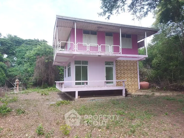 Charming two-story pink house with balcony in lush green surroundings