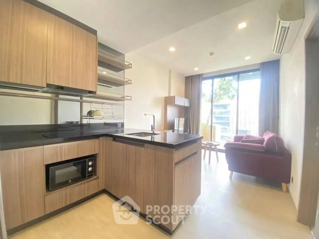 Modern open kitchen with sleek cabinetry and cozy living area, featuring large windows and natural light.