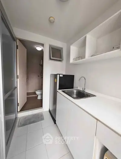 Compact kitchen with sleek white cabinetry and modern appliances, leading to a bathroom.
