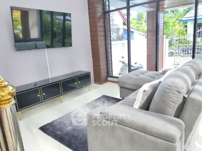Modern living room with sleek furniture and large TV, featuring natural light and stylish decor.