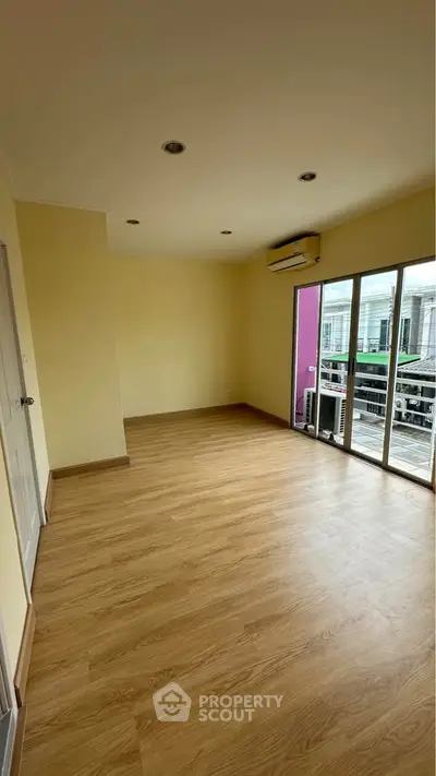 Spacious empty room with wooden flooring and large windows offering natural light.