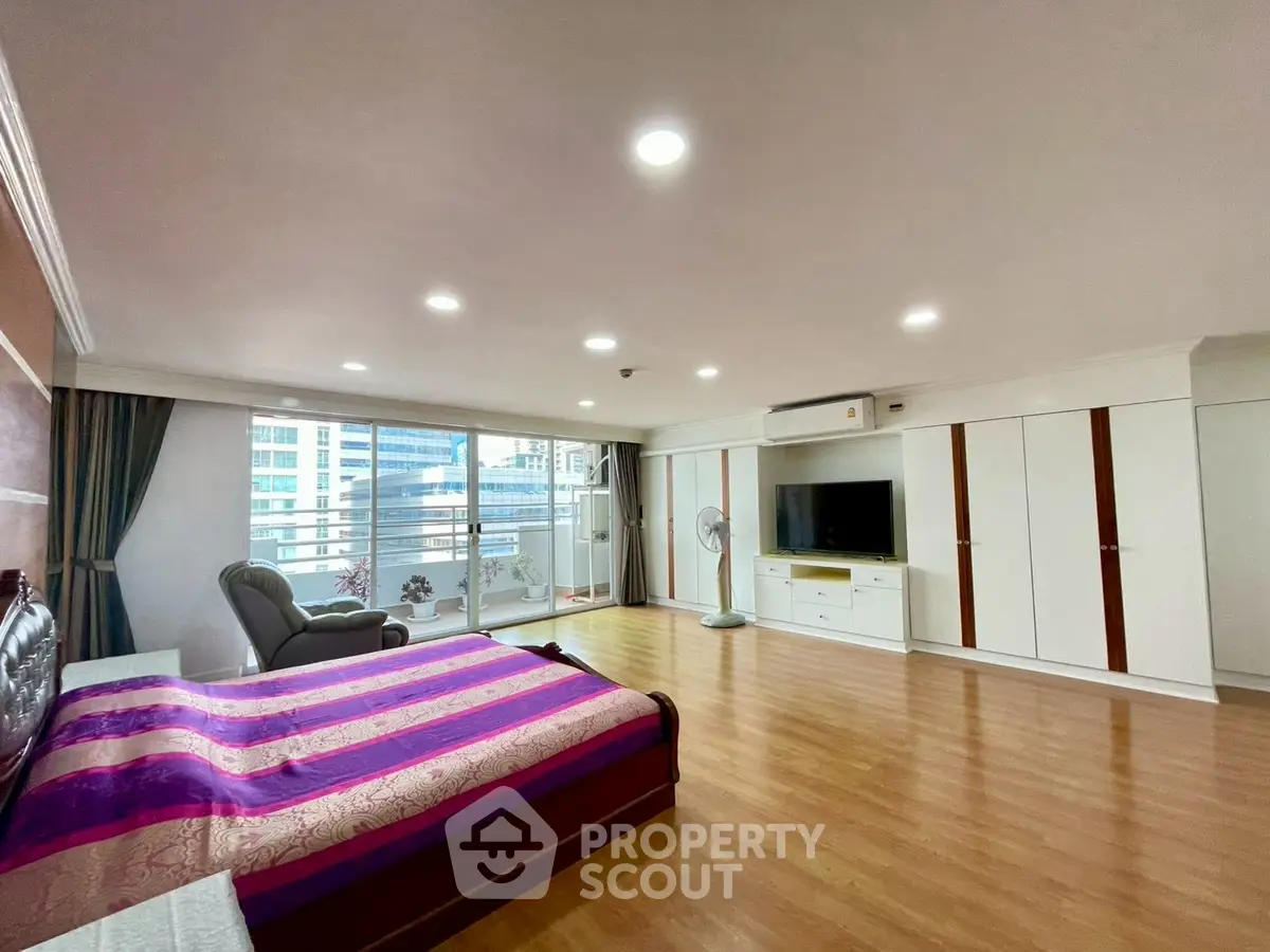 Spacious bedroom with large windows and modern furnishings in a high-rise apartment.