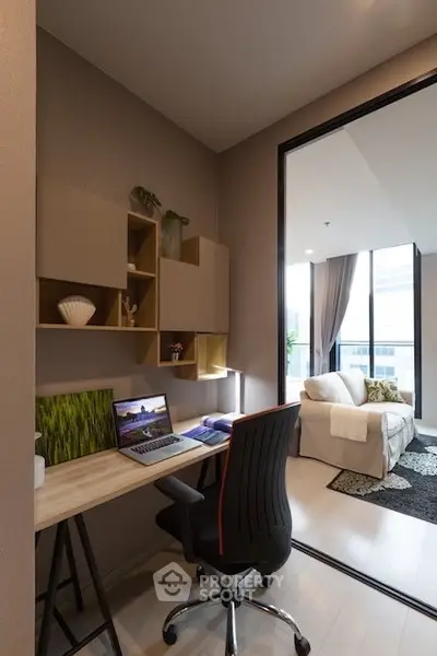 Modern study area with desk and chair leading to a cozy living room with large windows.