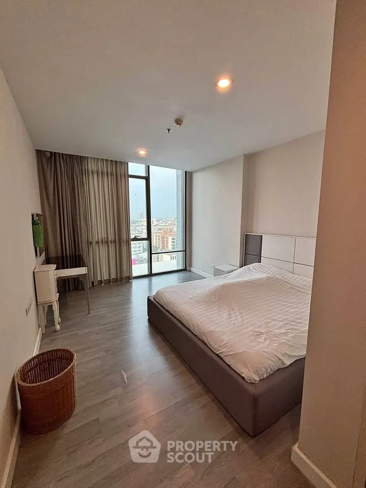 Spacious bedroom with city view and modern furnishings in a high-rise apartment.