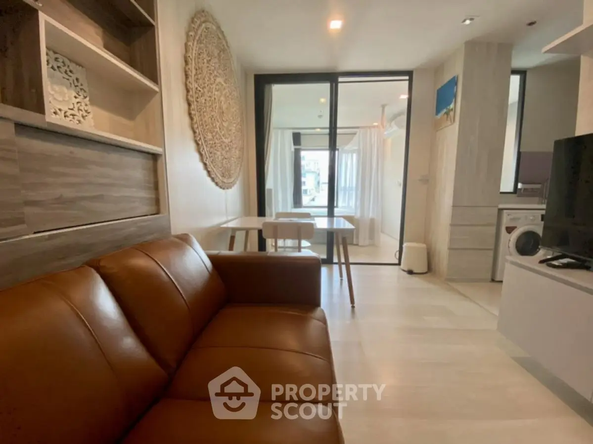 Modern living room with leather sofa and open layout leading to dining area and washing machine.