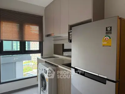 Modern kitchen with washing machine and fridge, featuring sleek cabinetry and large window view.