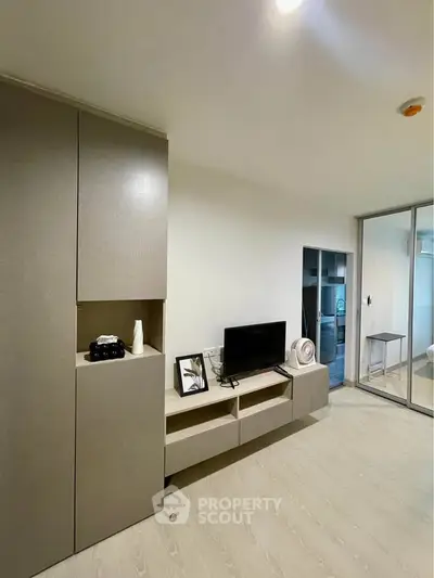 Modern living room with sleek storage and TV unit, featuring minimalist decor and sliding glass doors.