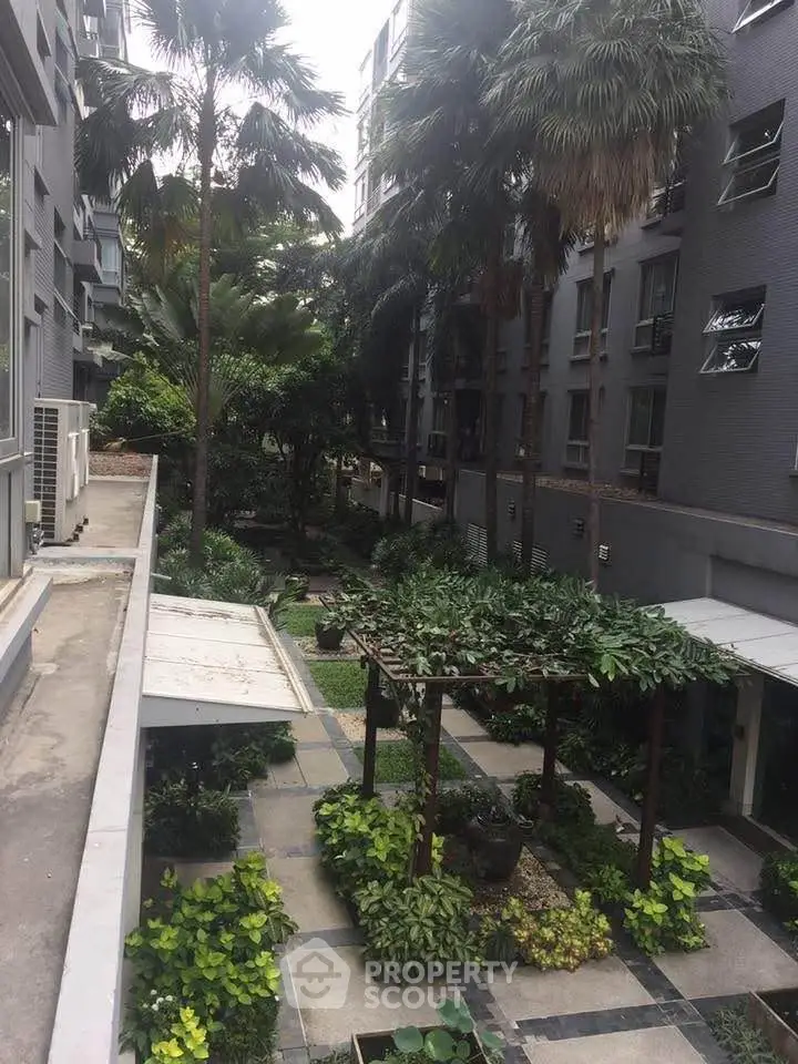 Lush garden courtyard in modern apartment complex with tropical plants and paved walkways.
