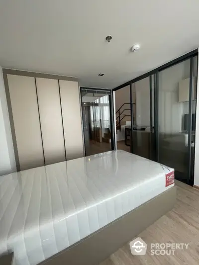 Spacious bedroom with large bed and mirrored wardrobe, leading to a modern glass-enclosed study area and an inviting living space.