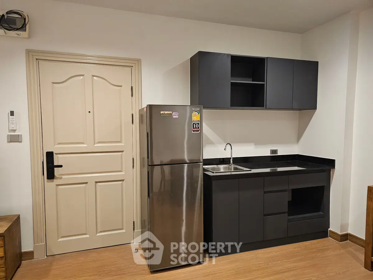 Modern kitchen with sleek cabinets and stainless steel fridge in compact apartment.