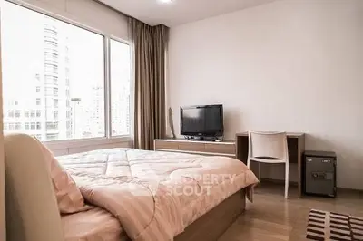 Modern bedroom with large window and city view, featuring a cozy bed and a small desk with a TV.