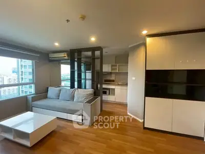 Modern living room with open kitchen and city view, featuring sleek furniture and wooden flooring.