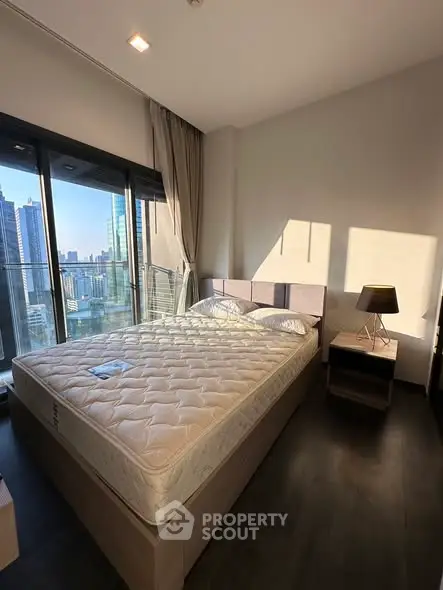 Modern bedroom with city view, featuring a large bed and floor-to-ceiling windows in a high-rise apartment.