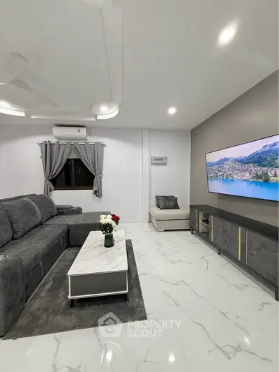 Modern living room with sleek gray sofa, marble coffee table, and wall-mounted TV in stylish apartment.