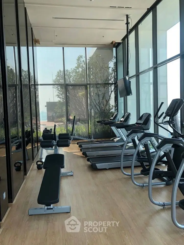Modern gym with large windows and state-of-the-art equipment in luxury building.
