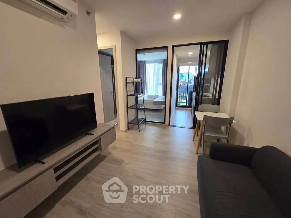Modern living room with sleek furniture and open layout leading to a cozy bedroom.