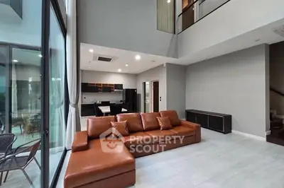 Spacious modern living room with high ceilings and open kitchen layout, featuring a large leather sofa and floor-to-ceiling windows.