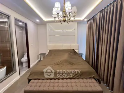 Luxurious bedroom with elegant chandelier and en-suite bathroom in modern apartment.