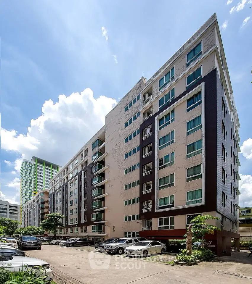 Modern multi-story residential building with parking area and clear blue sky.
